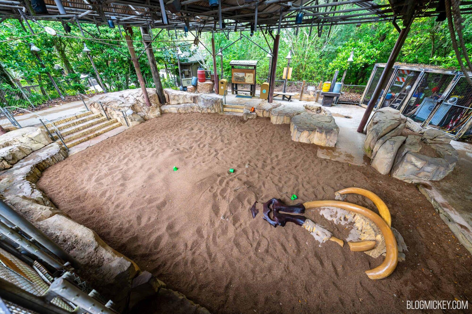 Covered sand playground area called "The Dig Site" with rocks, sand, and partially uncovered fossil bones, ready for children's play and family fun.