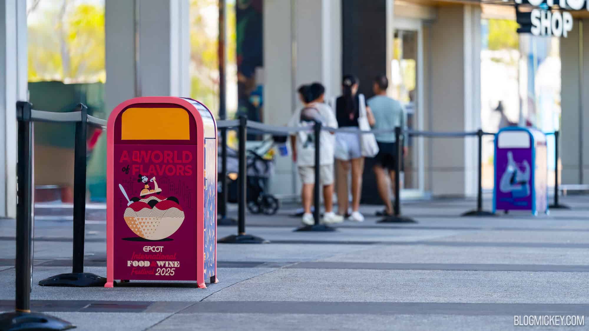Colorful trash can for EPCOT International Food & Wine Festival 2025 at Disney World, with guests waiting in line outside the entrance.