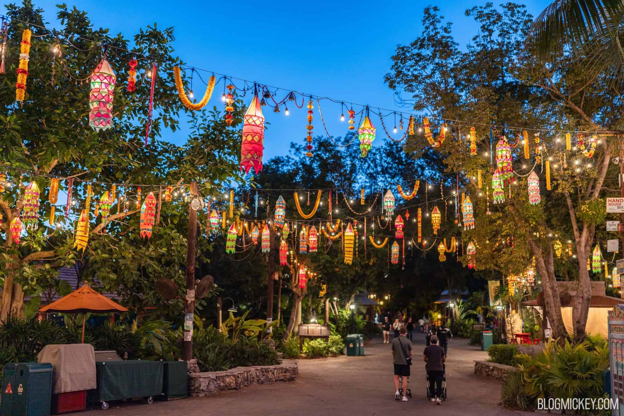 Colorful lanterns and string lights hanging above a park pathway at dusk.