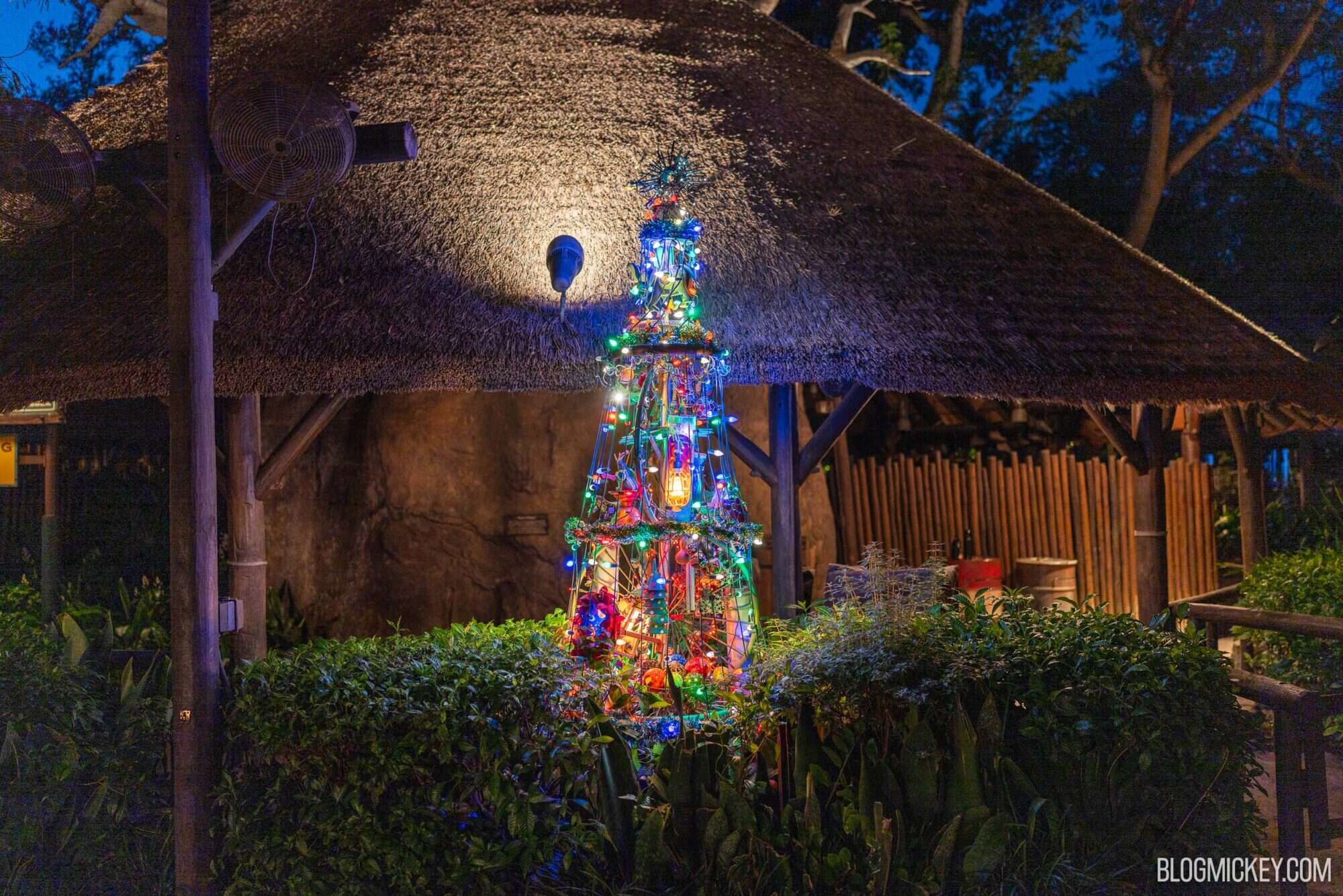 Colorful Christmas tree decorated with lights under thatched roof at Walt Disney World.
