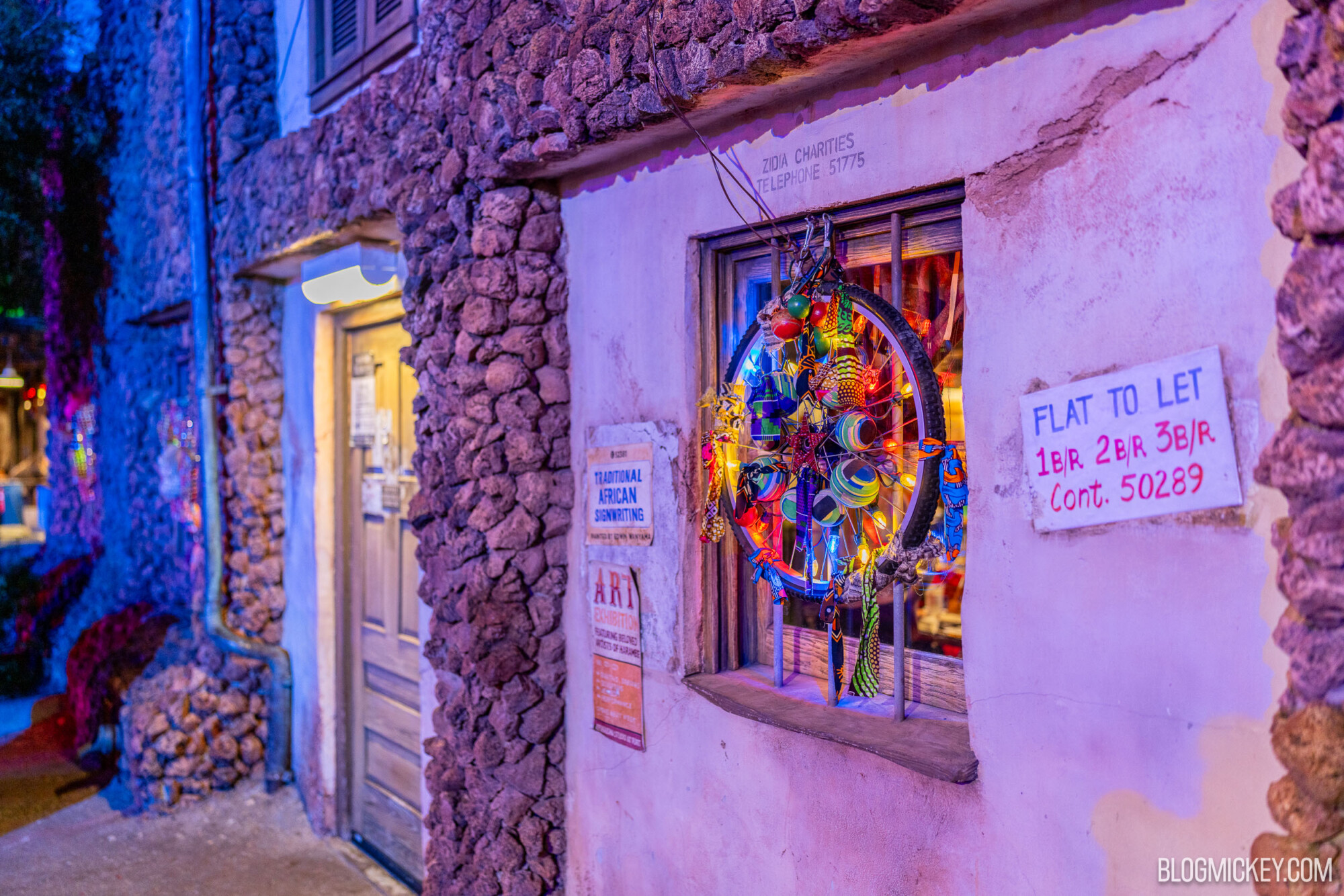 Colorful African art display in a rustic shop window at night.