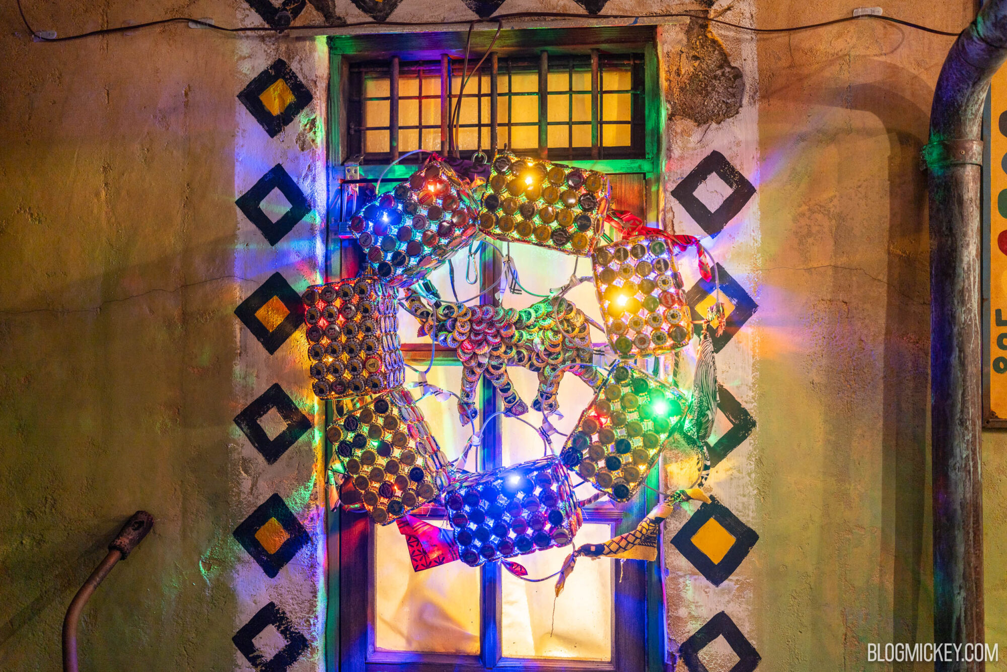Brightly lit colorful artistic light installation on a rustic wall with geometric patterns and a window.