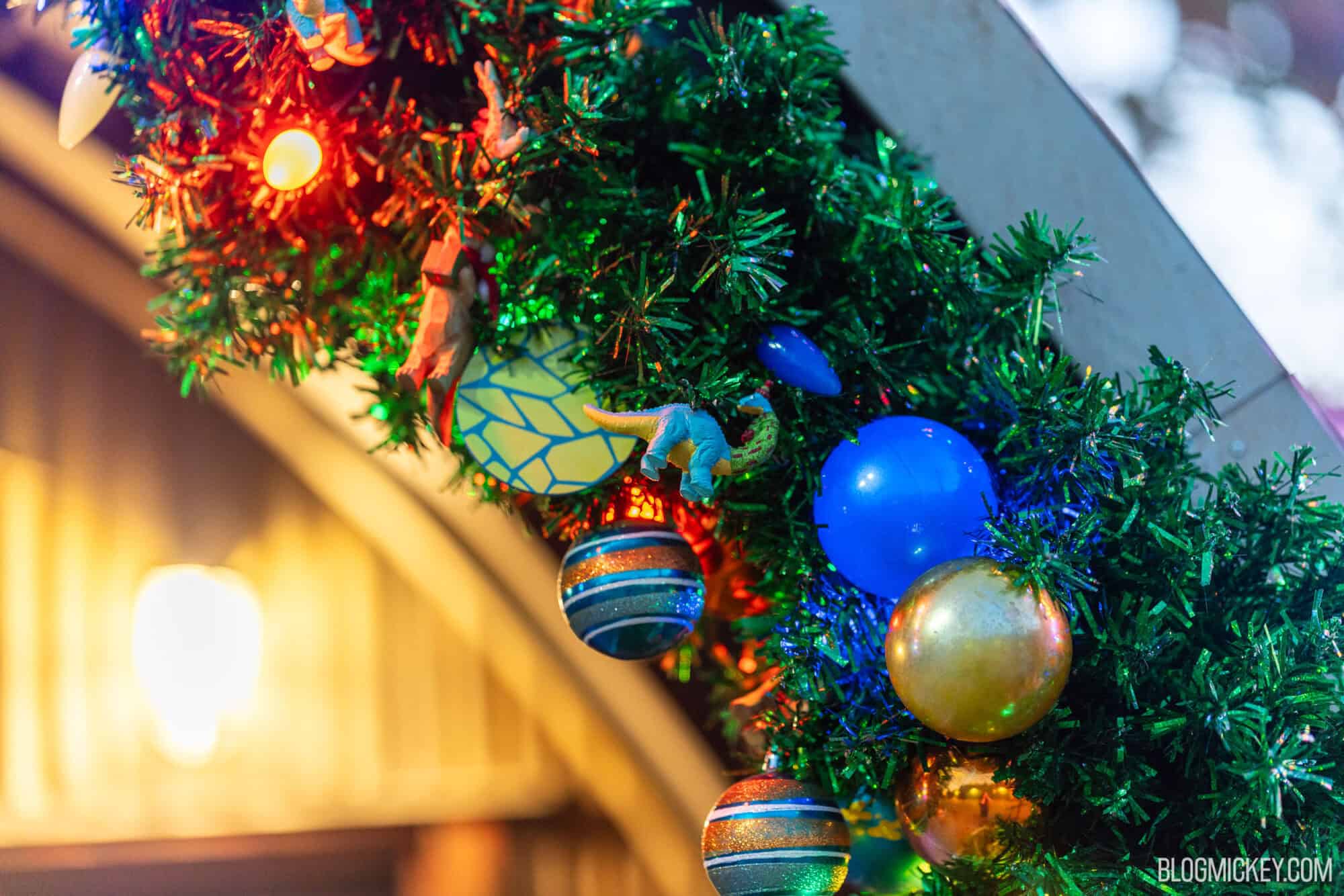 Colorful Christmas tree decorated with ornaments, lights, and dinosaur stickers at Disney.