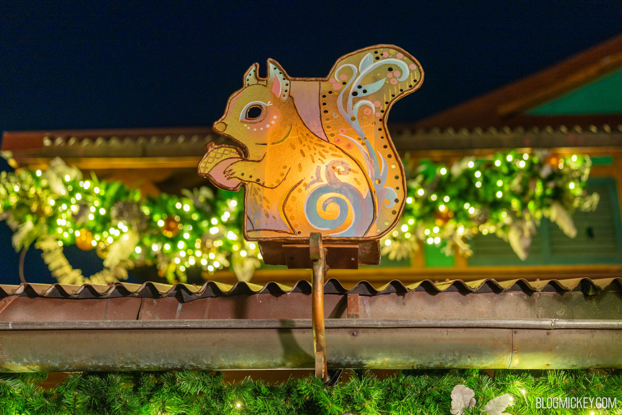 Colorful squirrel illuminated at a nighttime holiday display with festive greenery and lights.