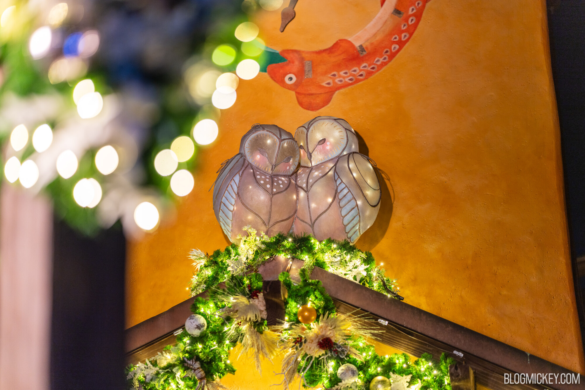 Colorful holiday decoration featuring illuminated bird figurines and festive greenery.