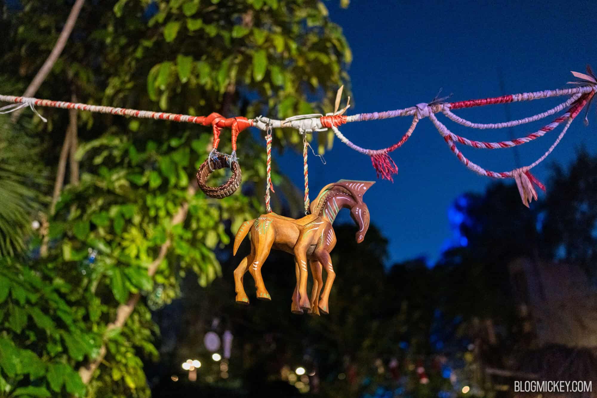 Colorful wooden animal wind chime hanging on a festive string at night.