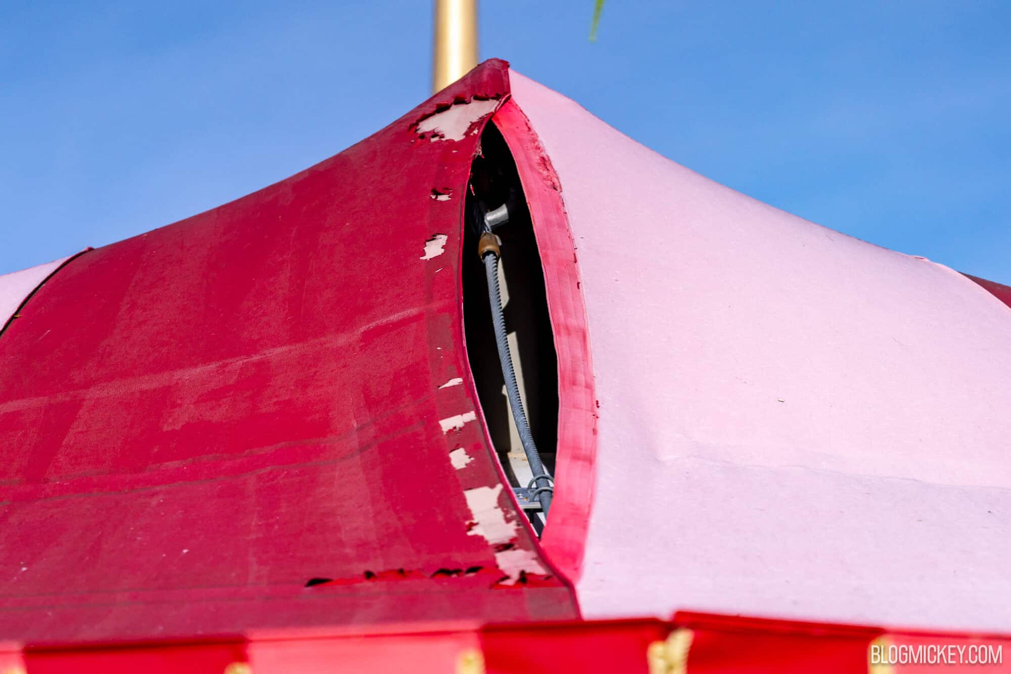 A worn red tent at Disney World with peeling paint and visible metal supports against a bright blue sky.