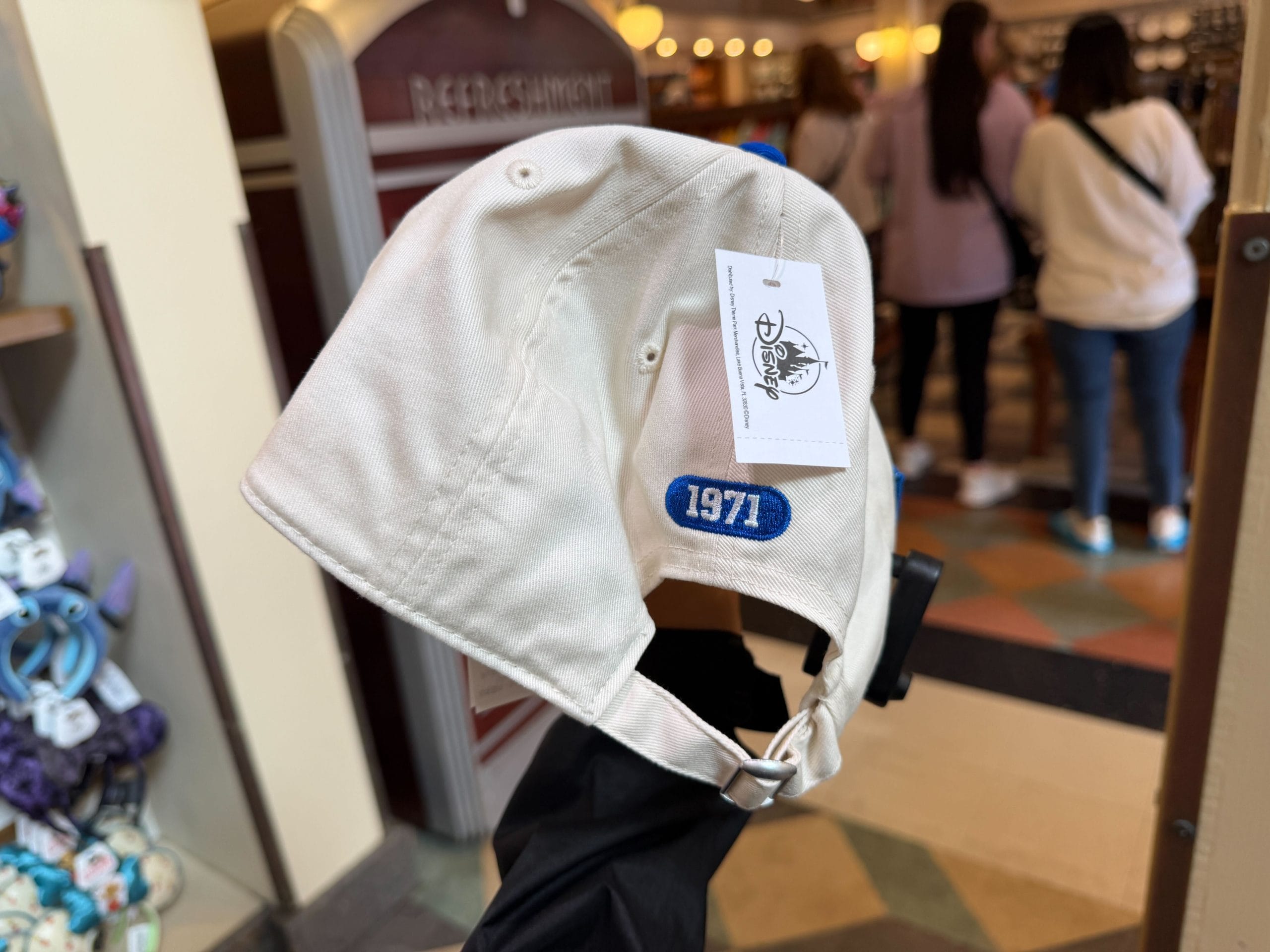 On the back of the hat, in the same royal blue, is an oval with "1971" cut out of it. The side of the hat features a patch with a vintage sports aesthetic Mickey Mouse. Beside him is a wavy circle with Cinderella Castle inside it and the words "Lake Buena Vista" and "Est. 1971." Beneath that is a tiny, vintage Disney World wordmark.