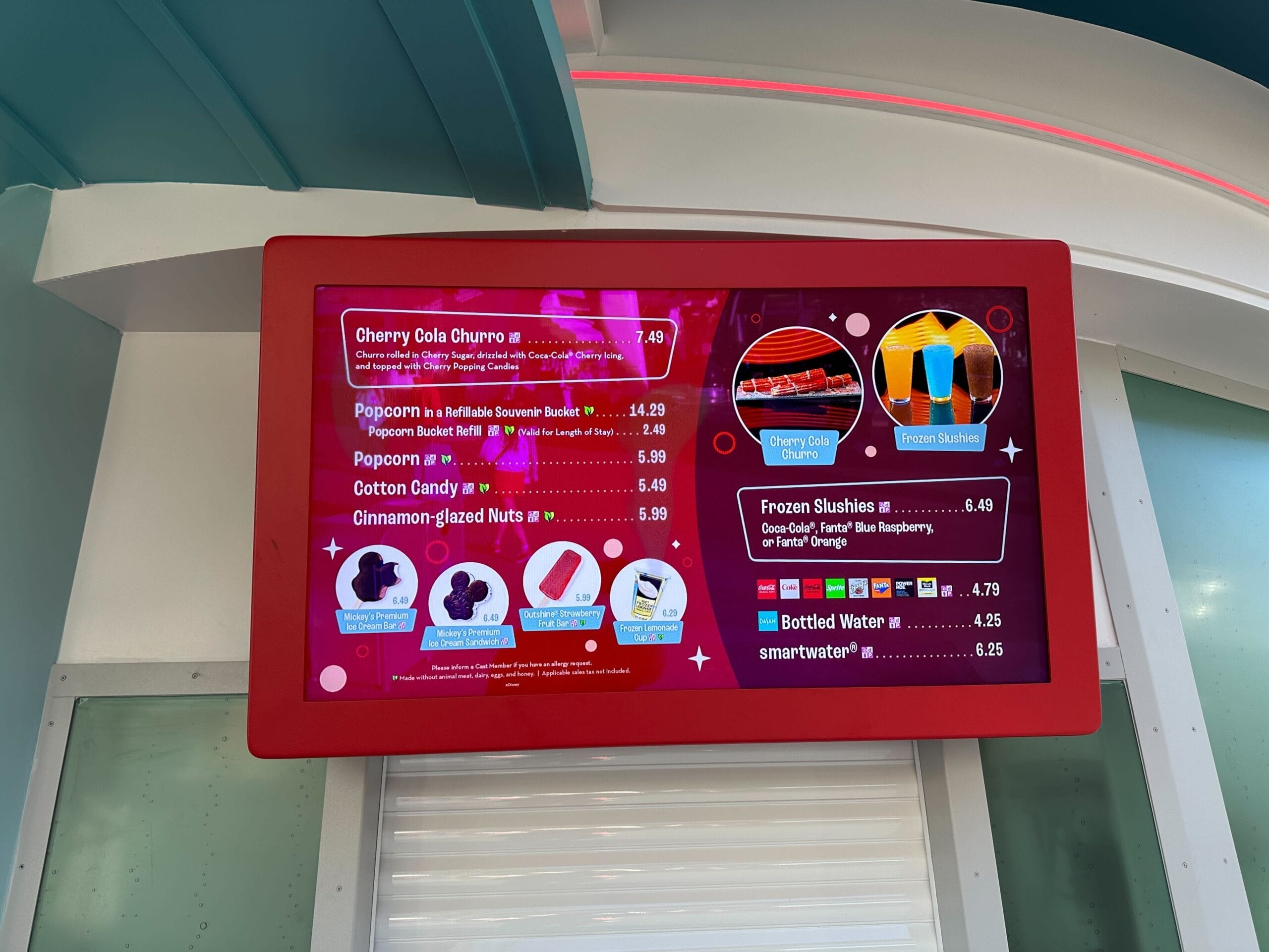 Red menu board at Magic Kingdom shows snacks like churros and popcorn; Cinderella Castle here is taller than Disneyland’s original.