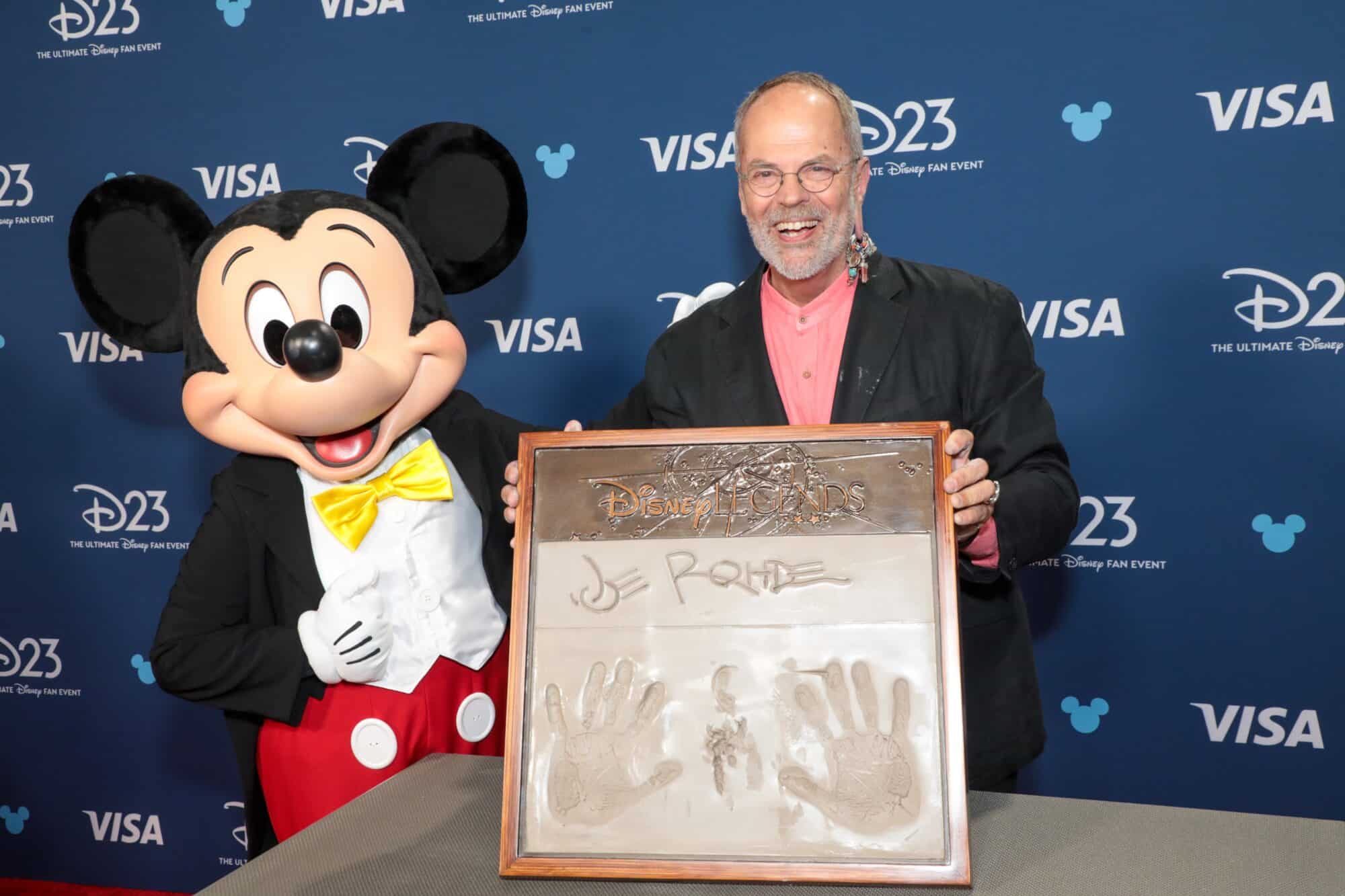 Mickey Mouse and Joe Rohde holding a Disney Legends handprint plaque at D23 event.